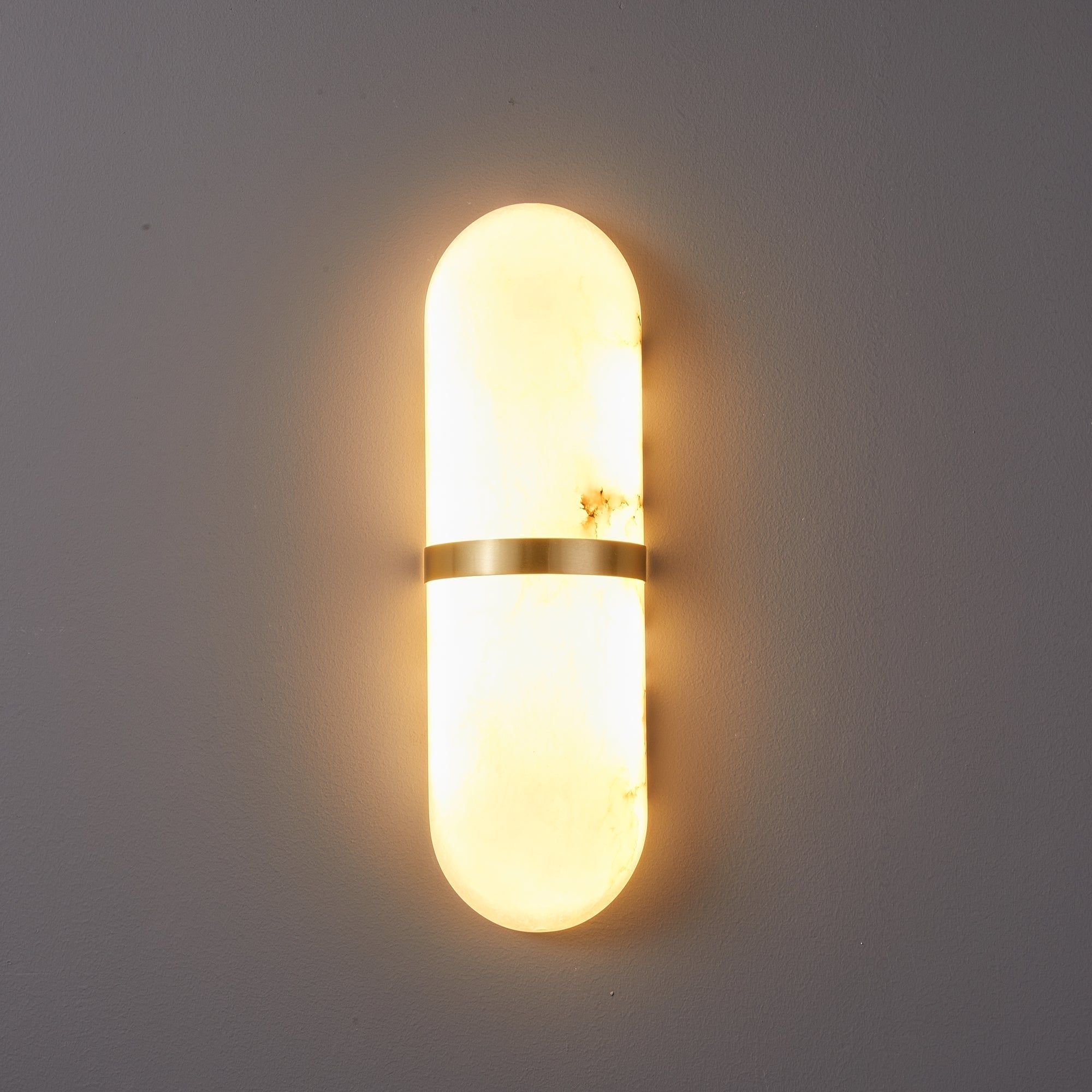 The Clérachic alabaster wall lamp lit head-on, brass band splitting the glow into upward and downward halves