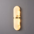 Clérachic wide alabaster wall lamp lit on a grey wall, brass band with light spilling above and below
