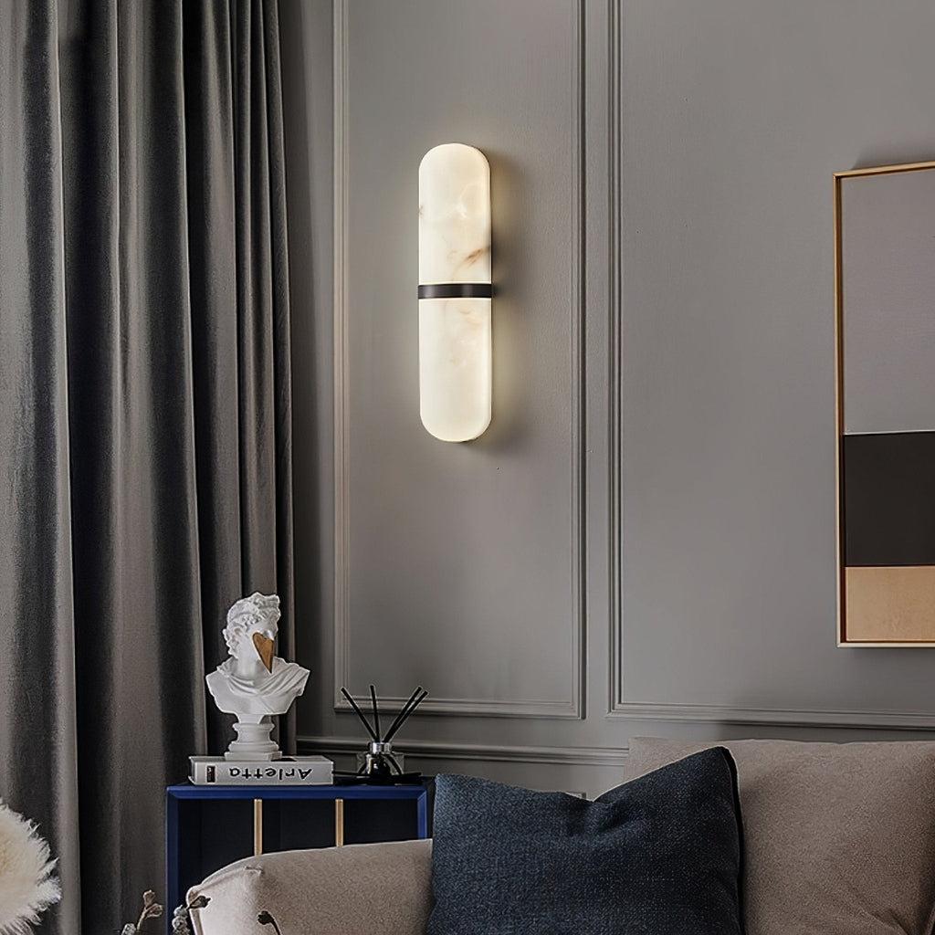 Clérachic black-banded alabaster wall lamp lit on a grey panelled living-room wall beside velvet curtains