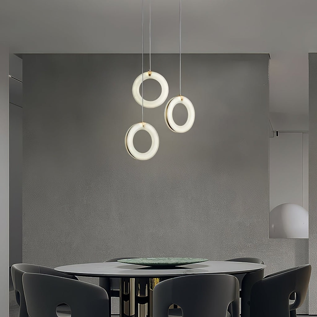 Wider view of a dining room with three alabaster ring pendants glowing above the round table