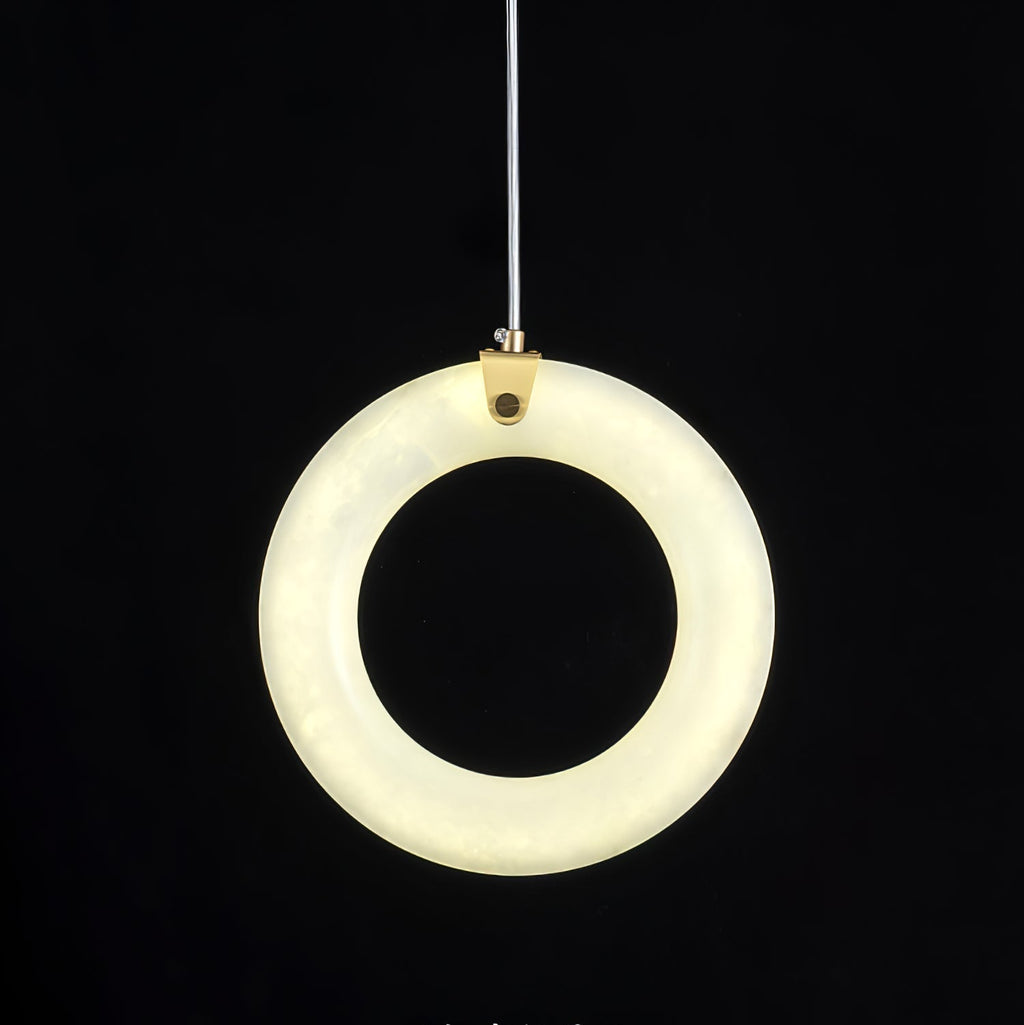 Alabaster ring pendant switched on against black, face-on, warm light spread evenly around the ring