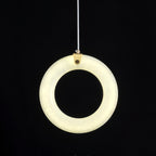 Alabaster ring pendant switched on against black, face-on, warm light spread evenly around the ring