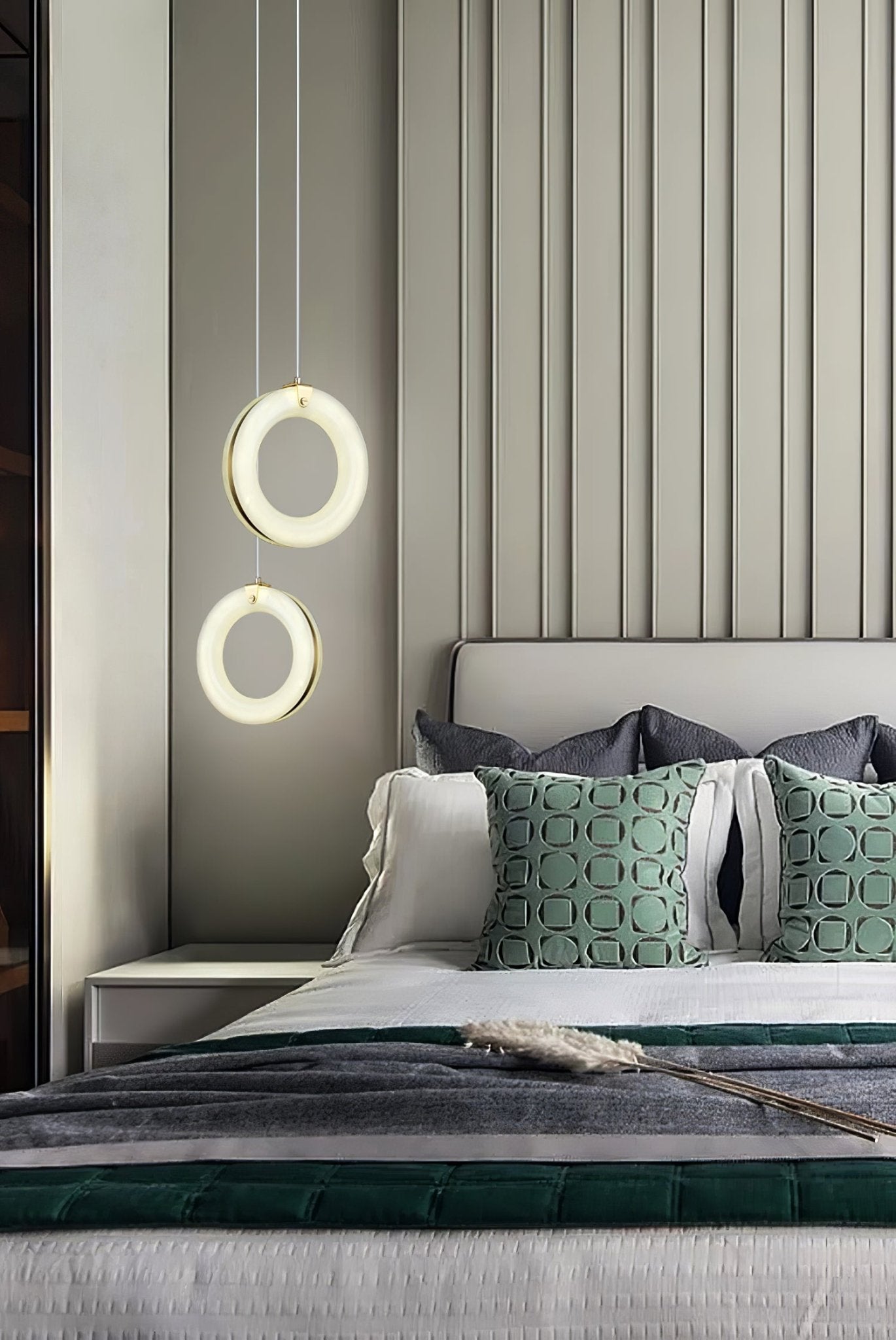 Two alabaster ring pendants at staggered heights beside a bed, lit above the nightstand