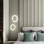 Pair of alabaster ring pendants hung one above the other next to a headboard and green cushions
