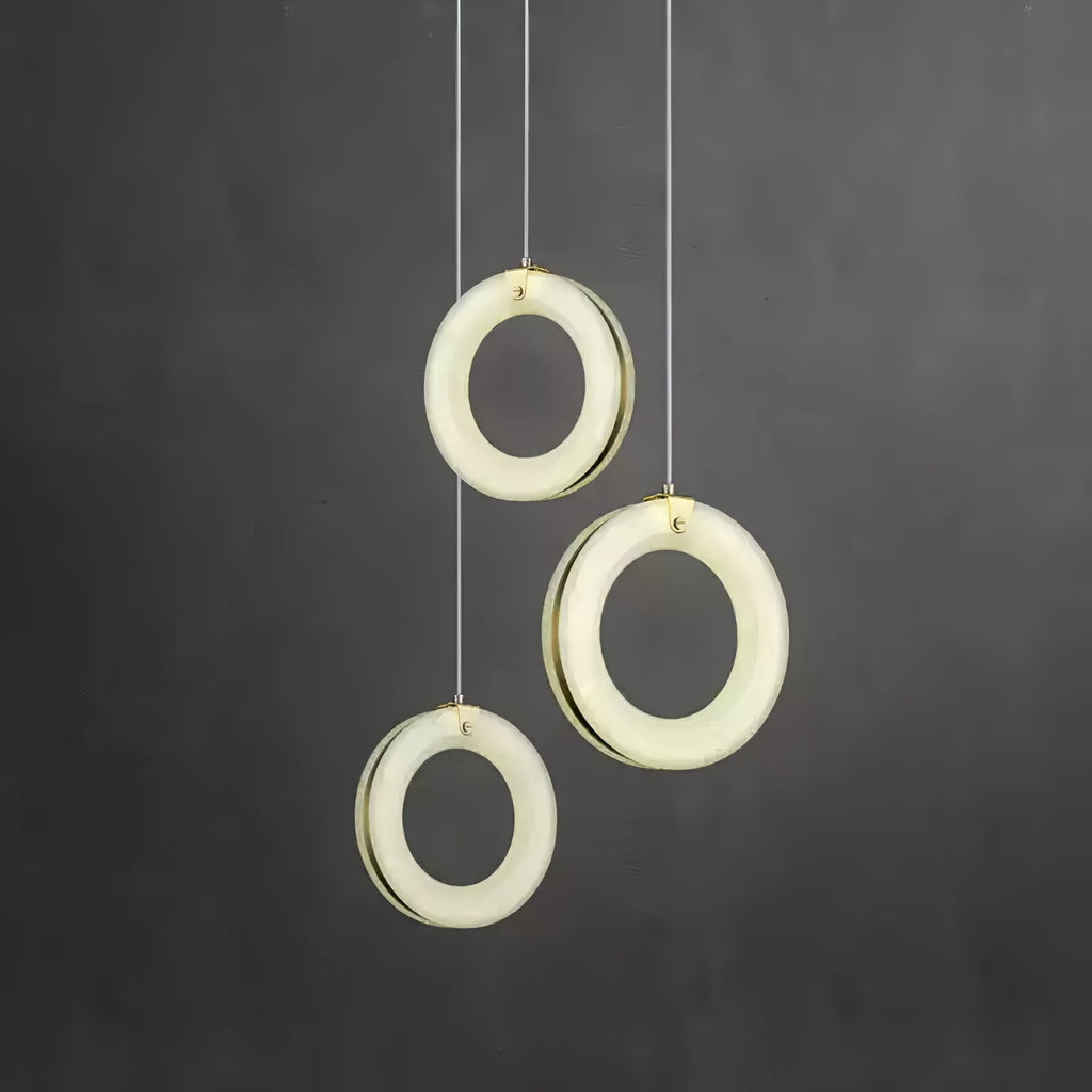 Three alabaster ring pendants staggered at different heights against a dark grey wall, switched on