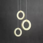 Three alabaster ring pendants staggered at different heights against a dark grey wall, switched on