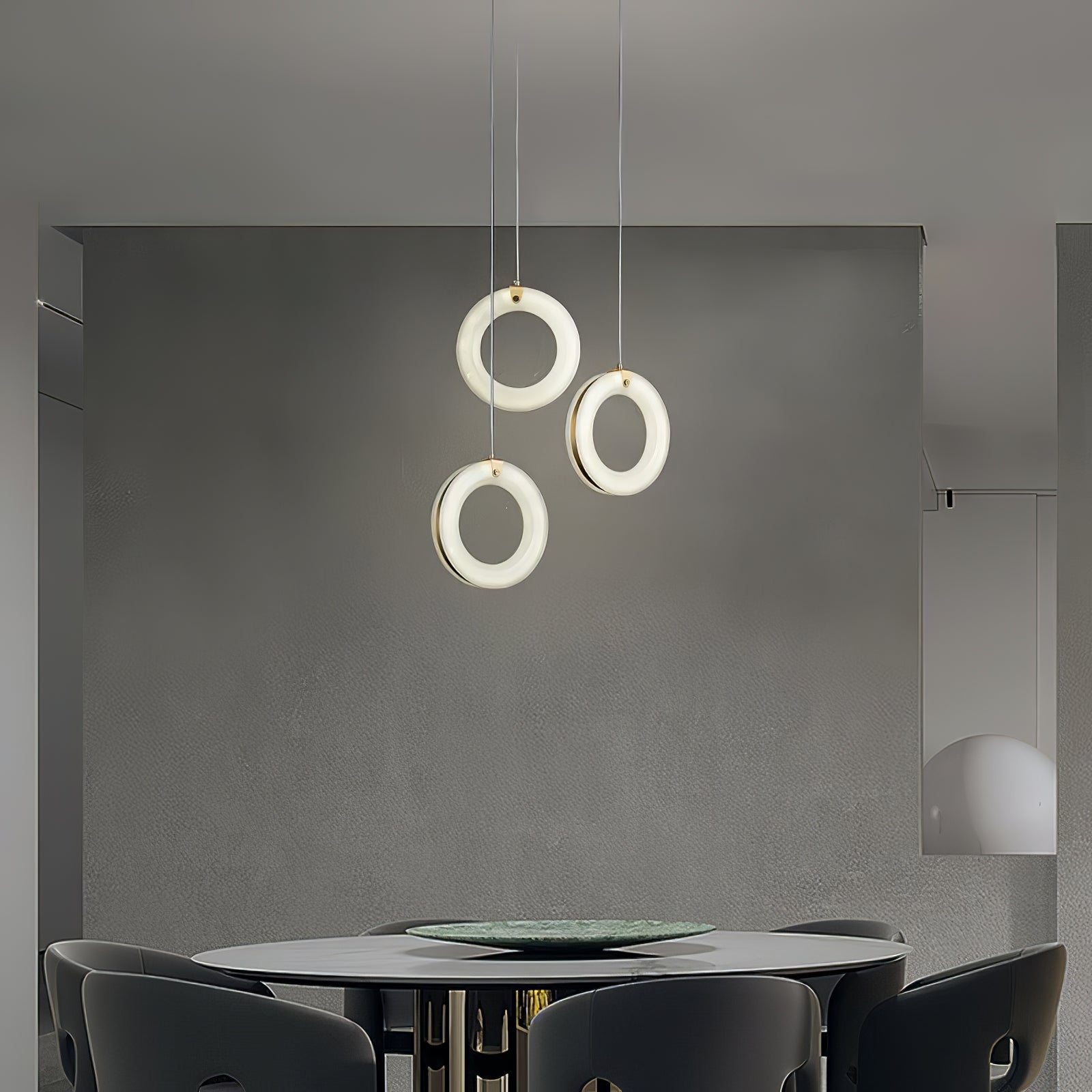 Three alabaster ring pendants clustered over a round dining table, warm light on a grey wall