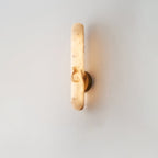 The sconce lit on cream, showing the full length of the rounded alabaster bar.