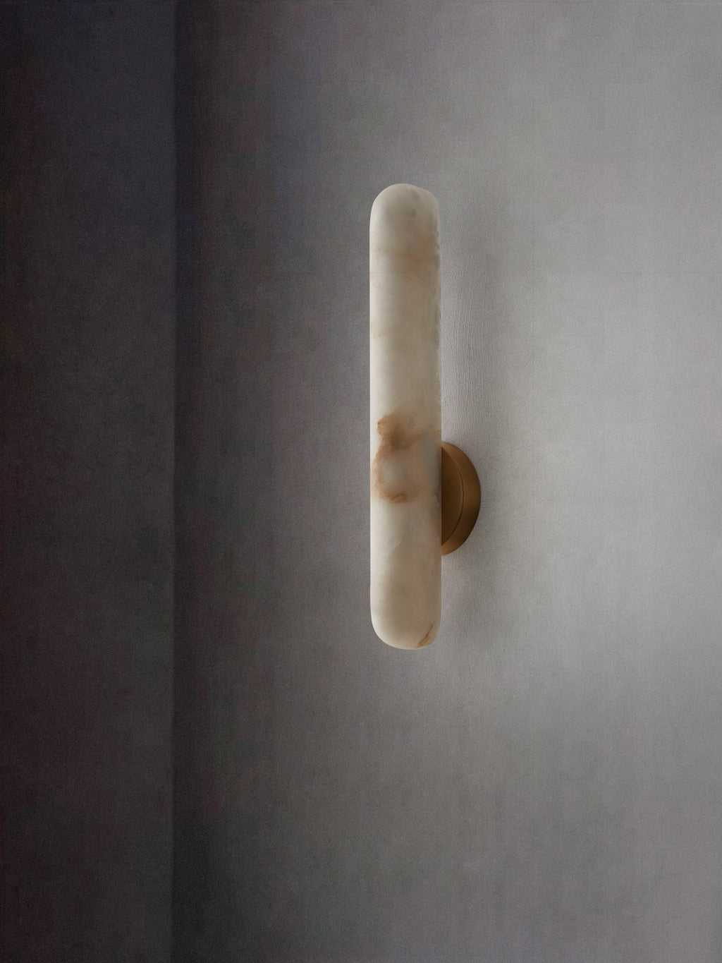 The unlit sconce on a soft grey wall, cool white stone with faint caramel markings.