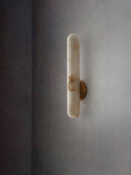 The unlit sconce on a soft grey wall, cool white stone with faint caramel markings.