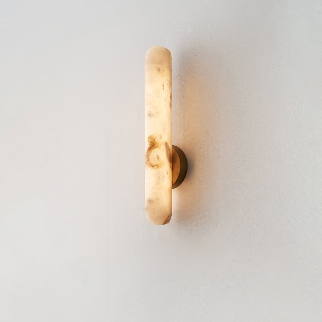 The lit sconce photographed on a plain cream wall, seen straight on from the front.