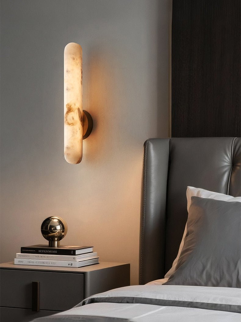 Lit above a bedside table stacked with books and a polished brass sphere ornament.