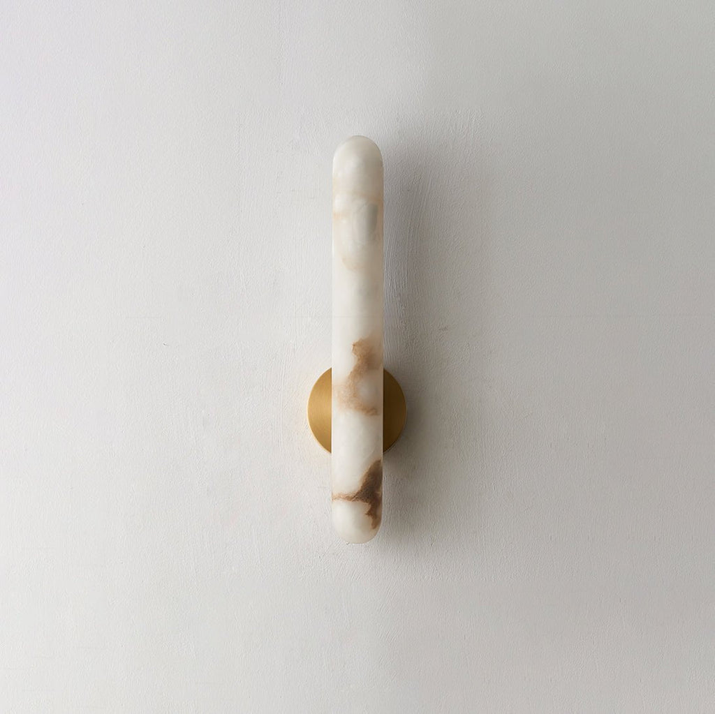 The unlit sconce on white, the brass mounting disc set against warm-veined stone.