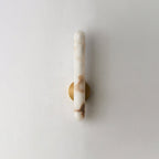 The unlit sconce on white, the brass mounting disc set against warm-veined stone.