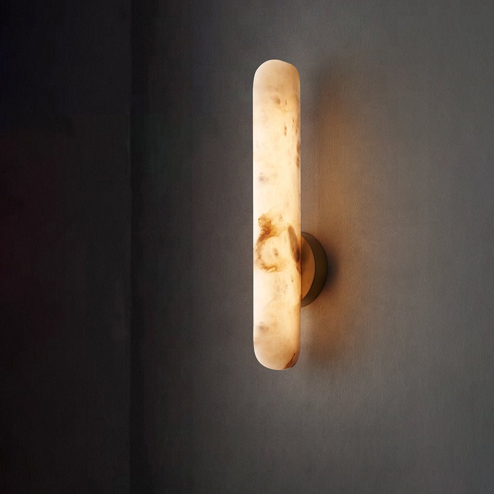 The sconce lit against a dark grey wall, warm light spilling from both ends of the bar.