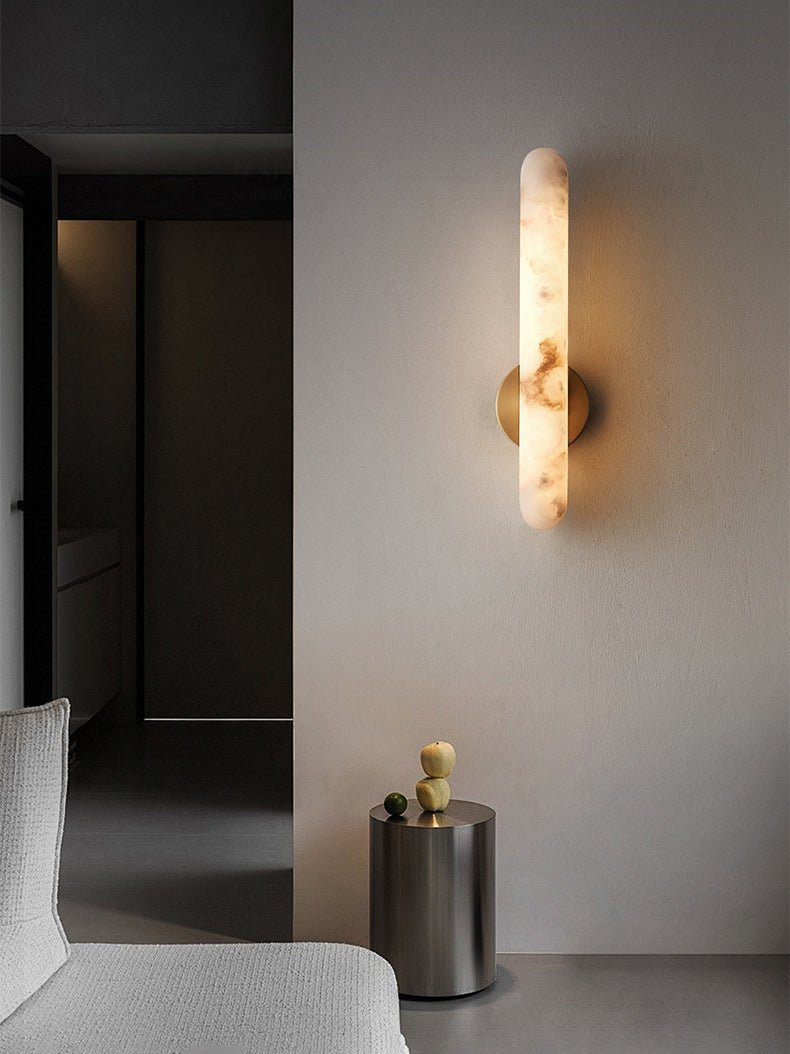 Lit on a pale wall beside a dark doorway, above a metal side table topped with small gourds.