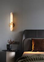 The sconce lit in a grey bedroom above a black side table holding dried stems in a stone pot.