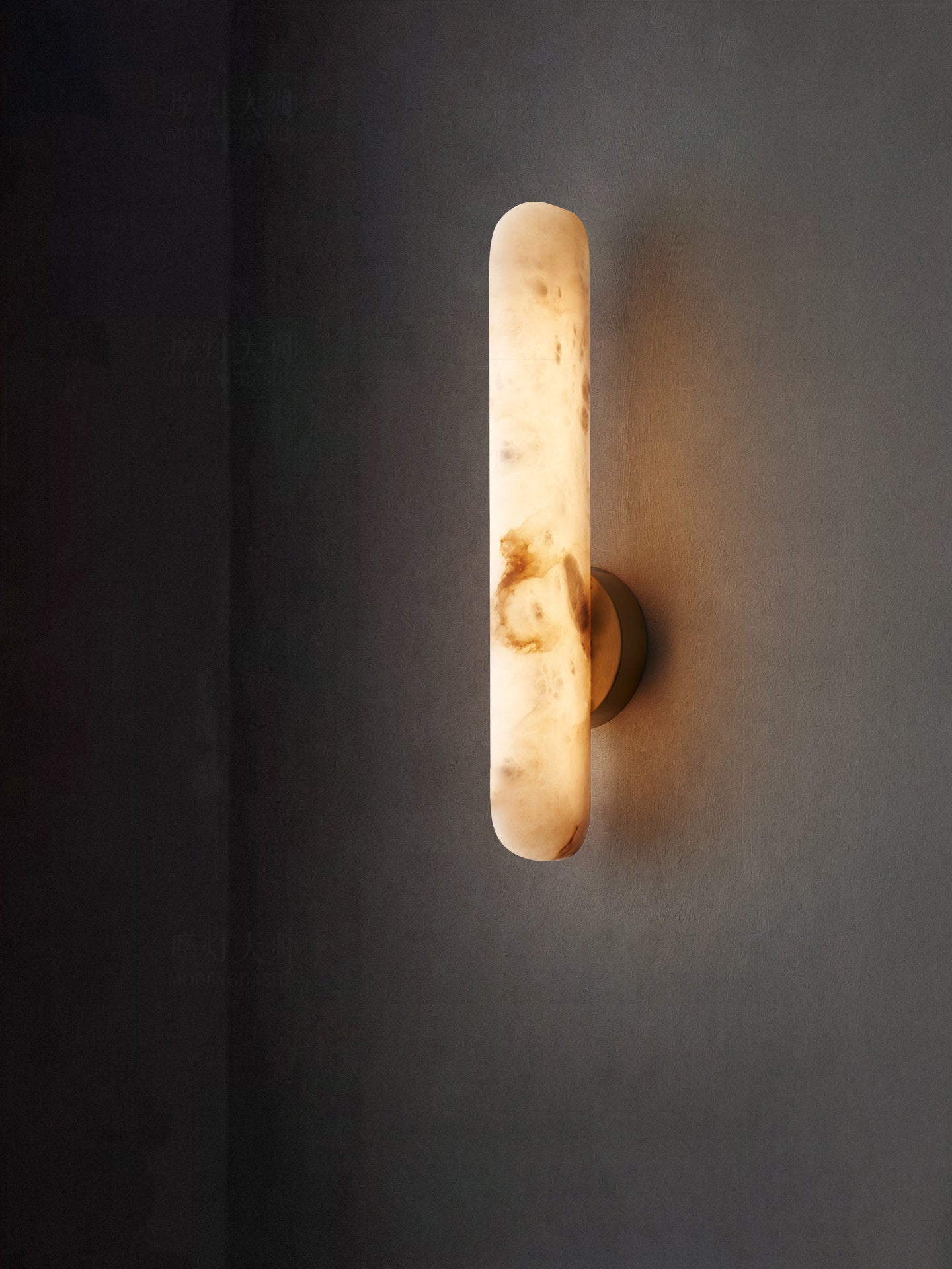 The lit rod sconce on a deep grey wall, its veining glowing amber through the alabaster.