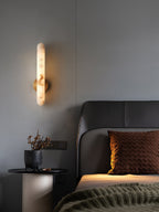 Lit beside a leather headboard, a black round table with dried flowers below the sconce.