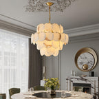 The chandelier lit in a grey classical dining room, beside a round mirror and marble fireplace.