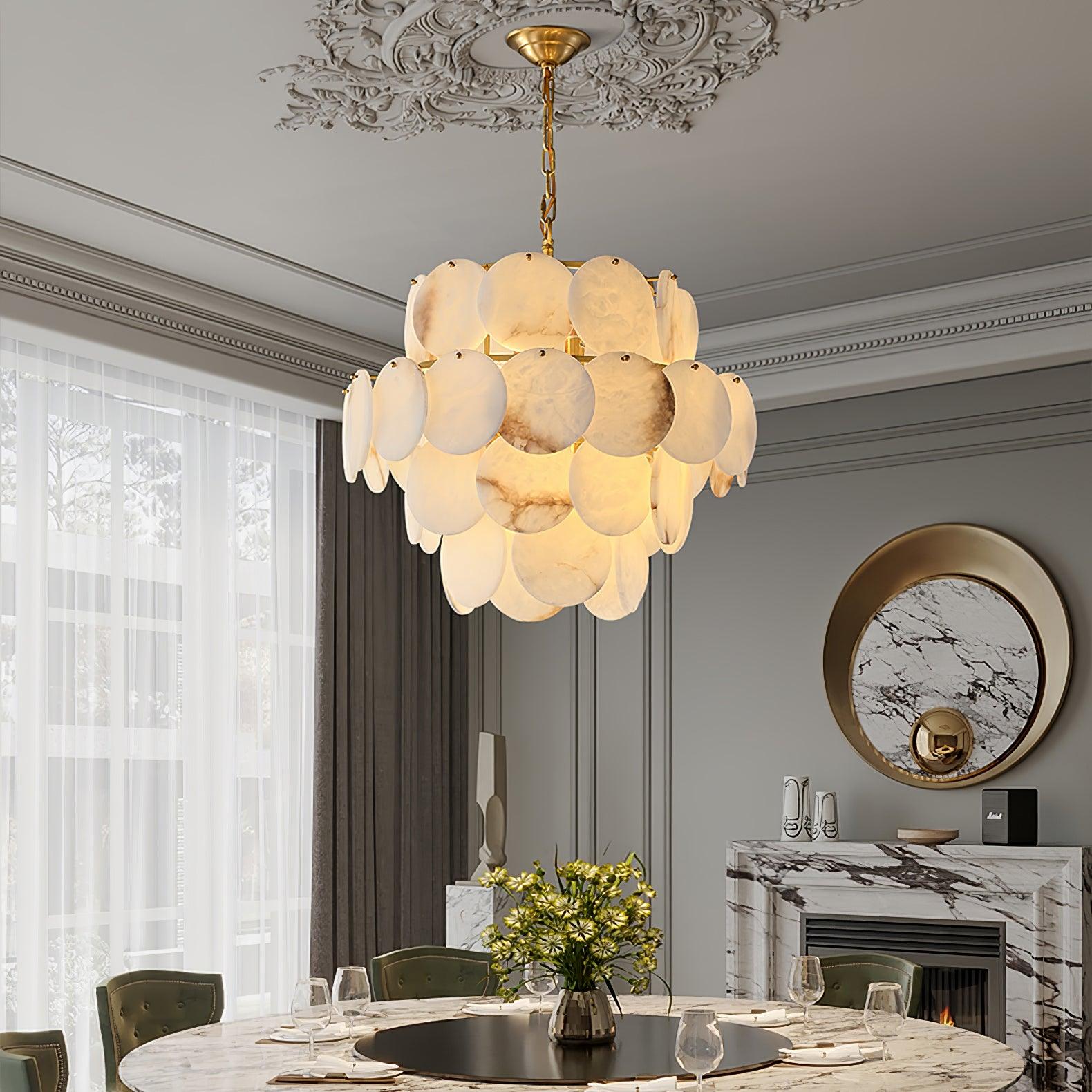 The chandelier lit in a grey classical dining room, beside a round mirror and marble fireplace.