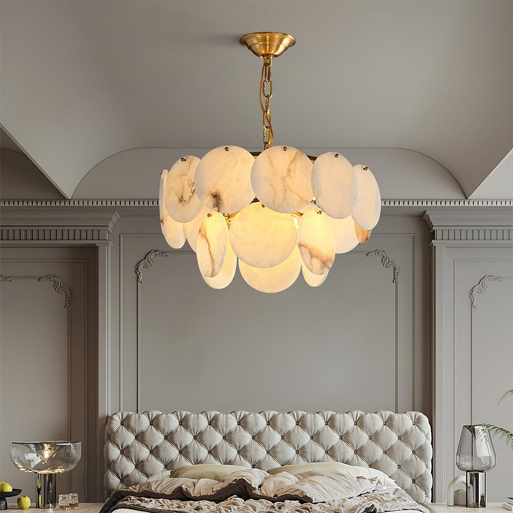 The chandelier lit in a bedroom above a grey tufted headboard, wall mouldings alongside.