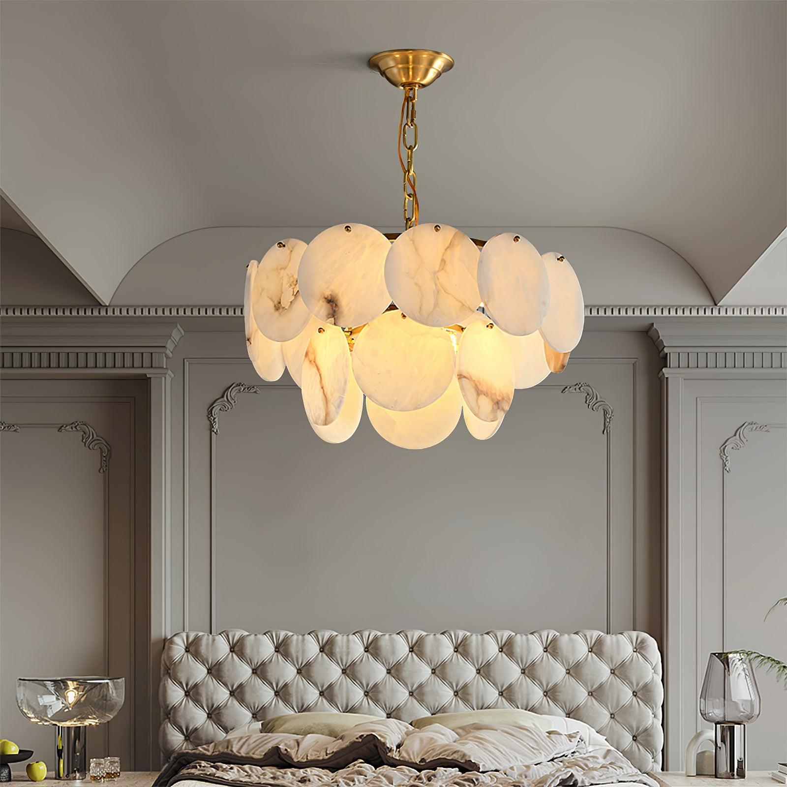 The chandelier lit in a bedroom above a grey tufted headboard, wall mouldings alongside.