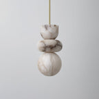 Alabaster totem pendant light unlit against a soft grey backdrop, brass rod above three stacked stone forms