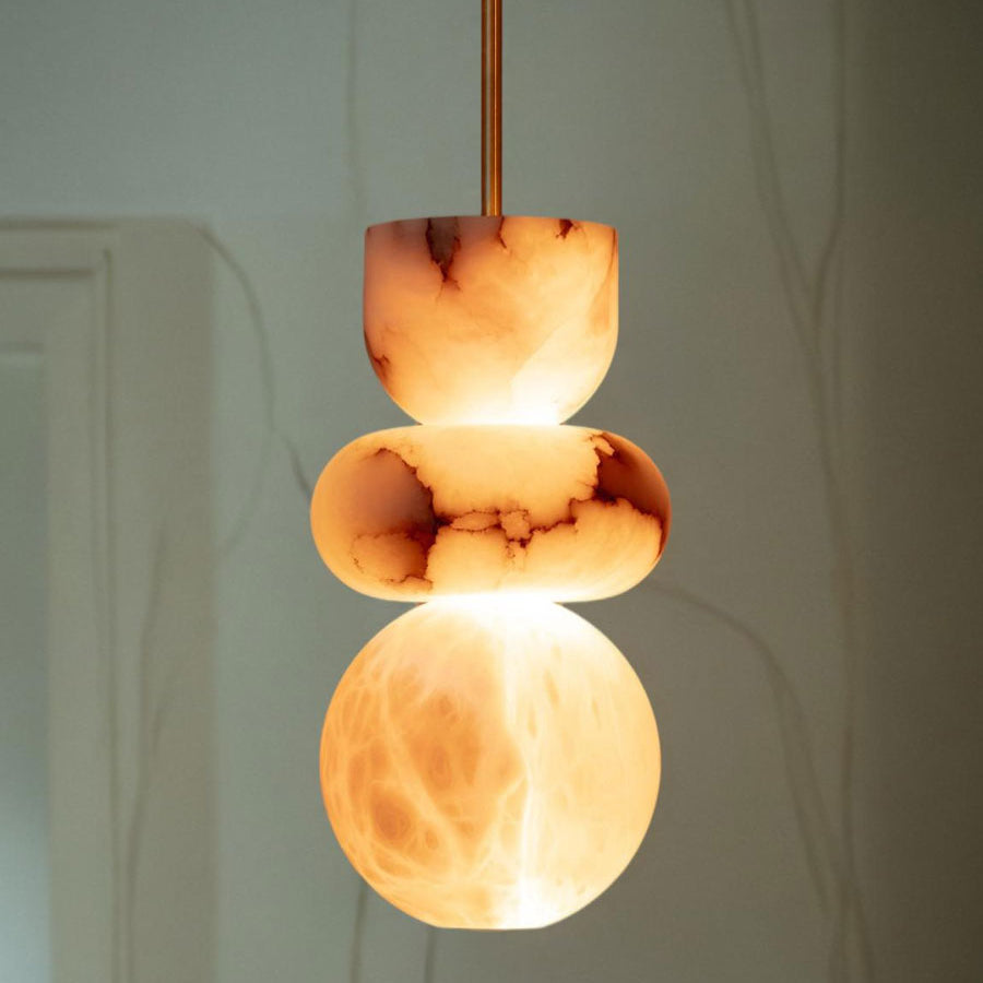 Lit alabaster totem pendant against a pale wall, branch shadows falling behind the glowing stone globe
