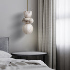 Unlit alabaster totem pendant hanging beside a bed and black side table in a daylit grey bedroom
