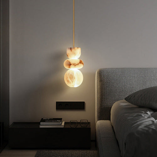 Alabaster totem pendant lit at night above a black nightstand beside an upholstered bed