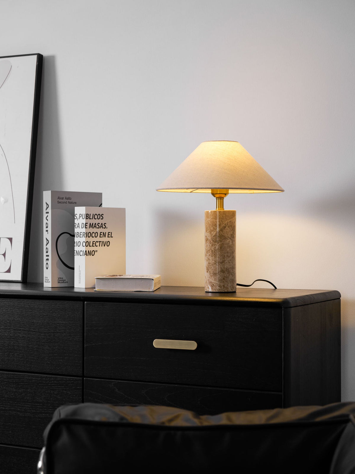 A black-and-white framed print leans against the wall beside the lit Clérachic table lamp and its stack of books on the dresser.