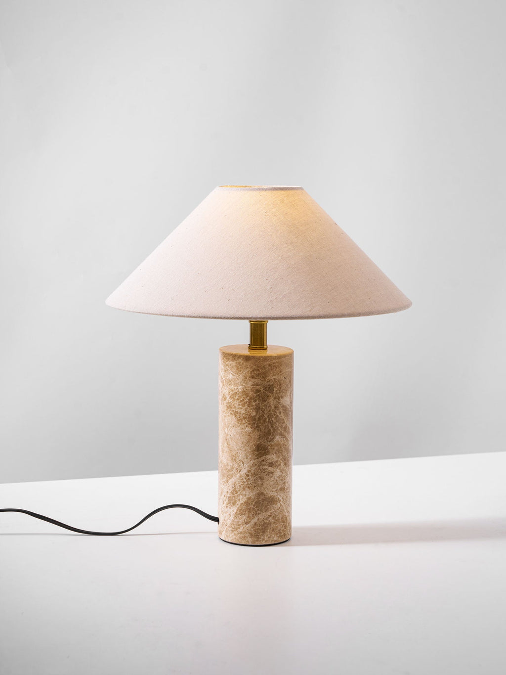 Another studio angle of the Clérachic table lamp, the shade lit at a slight tilt with the cord visible below.