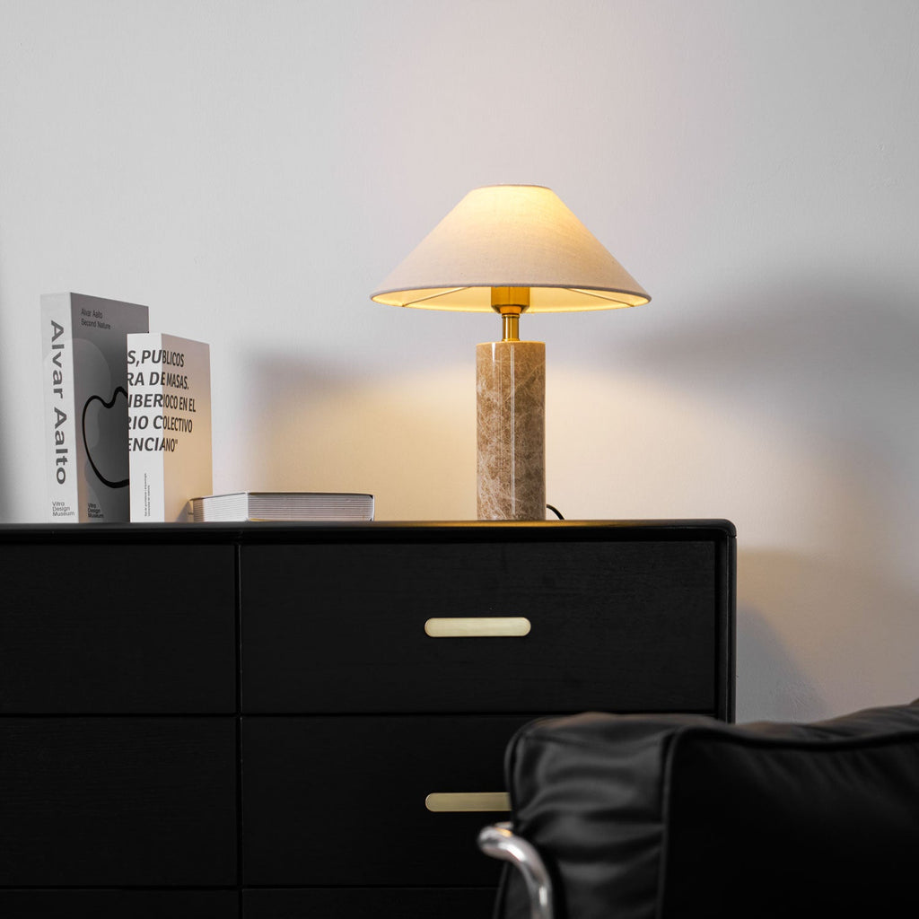 A closer crop of the same dresser scene, the Clérachic table lamp's shade glowing above the books and gold drawer pull.