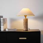 The Clérachic table lamp lit on a black dresser beside a stack of books and a black leather chair edge in the room's corner.