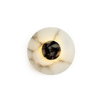 Clérachic rauduvyi wall lamp lit on a plain white background, warm light escaping around the marble centre