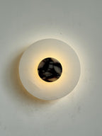 Clérachic rauduvyi wall lamp switched on, a ring of warm light glowing out from behind the marble centre disc