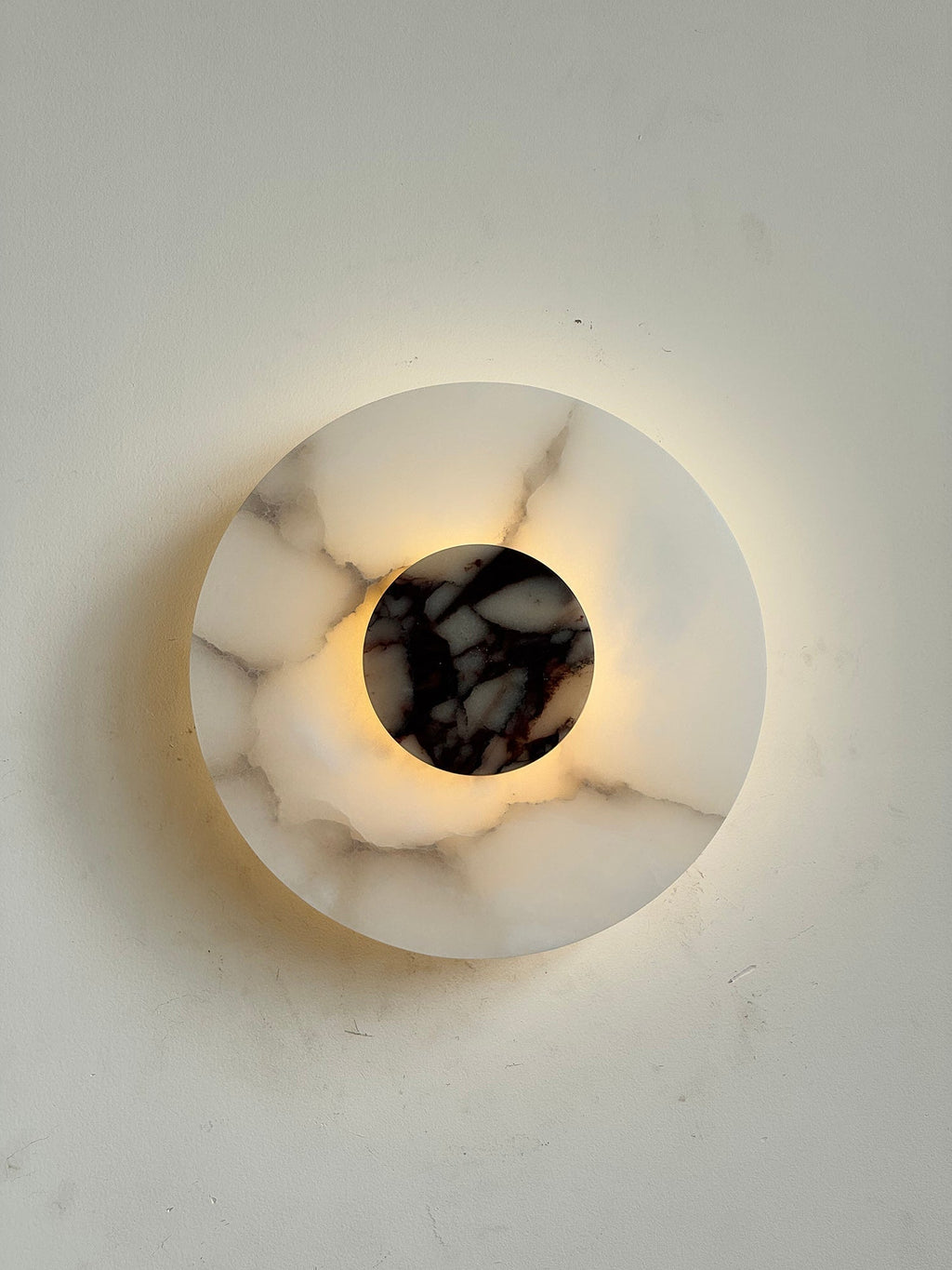 Clérachic lit Rauduvyi wall lamp whose translucent alabaster plate reveals grey veining as light passes through