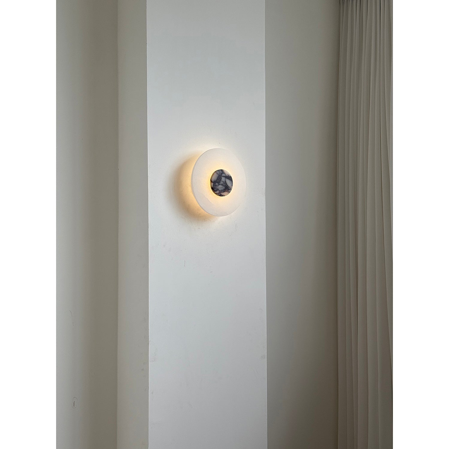 Clérachic rauduvyi wall lamp lit on a narrow wall pier beside floor-length pleated curtains