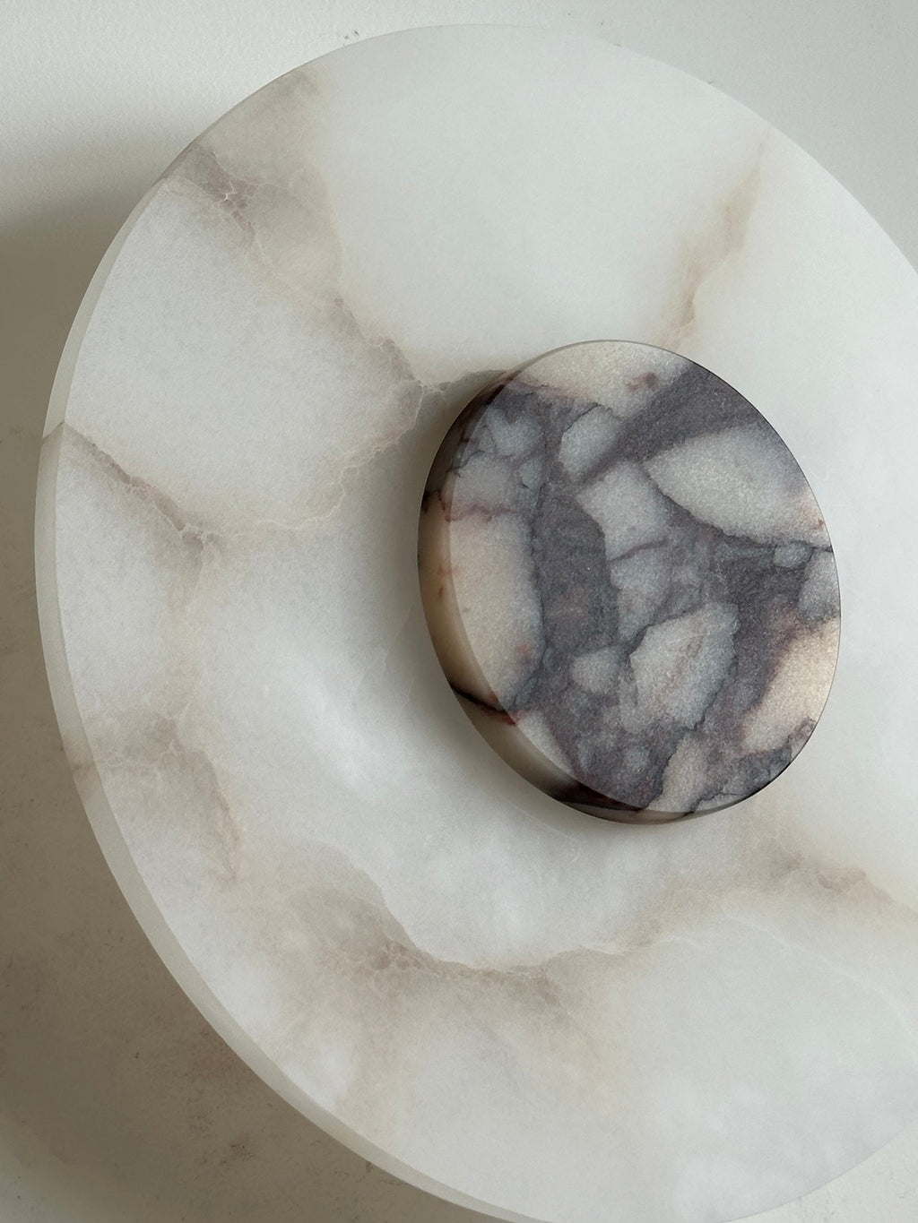 Clérachic angled close-up of the Rauduvyi wall lamp, marble disc raised above the veined alabaster backplate