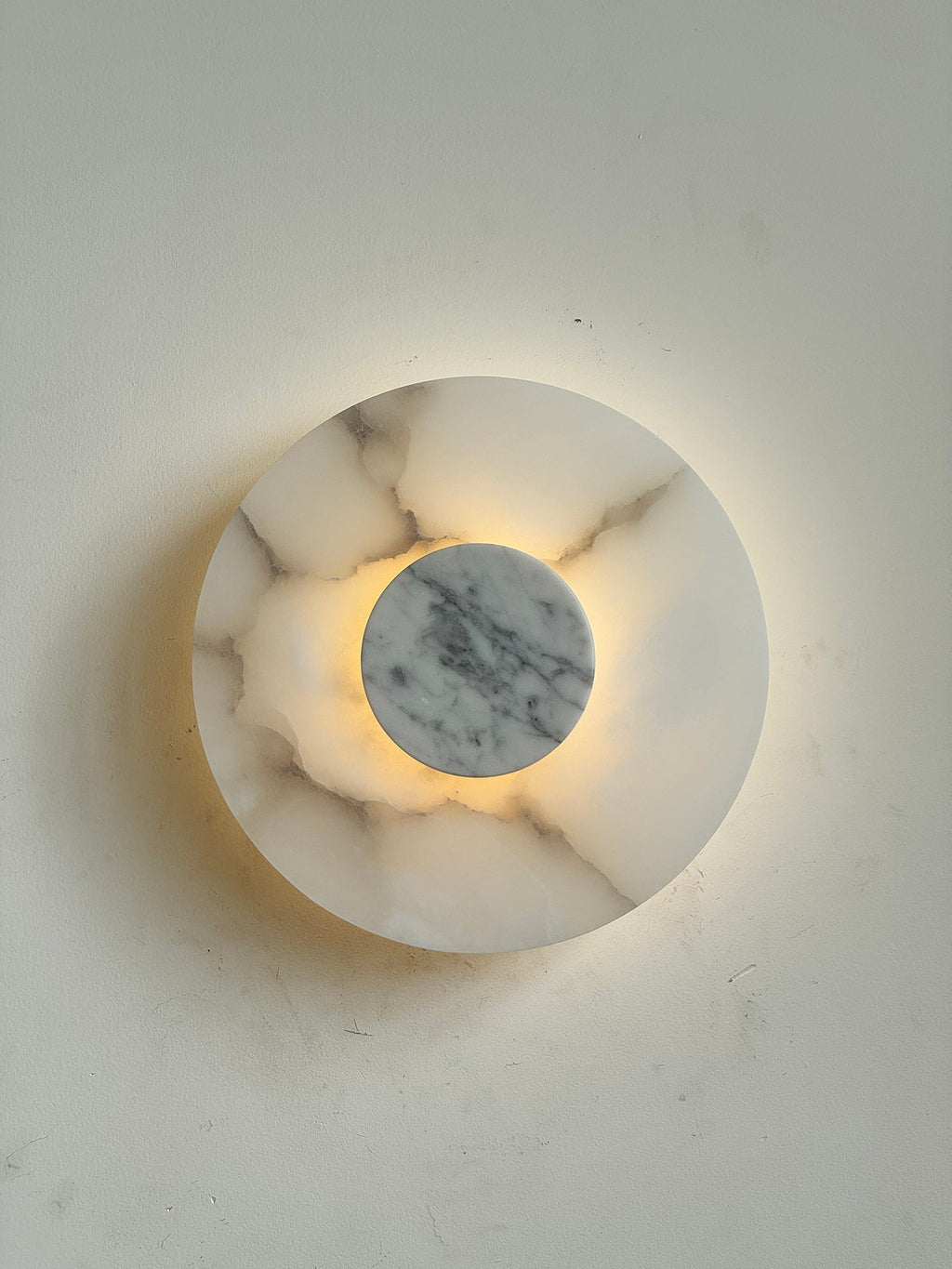 Clérachic rauduvyi wall lamp lit so the grey veining in the alabaster plate shows through the warm light