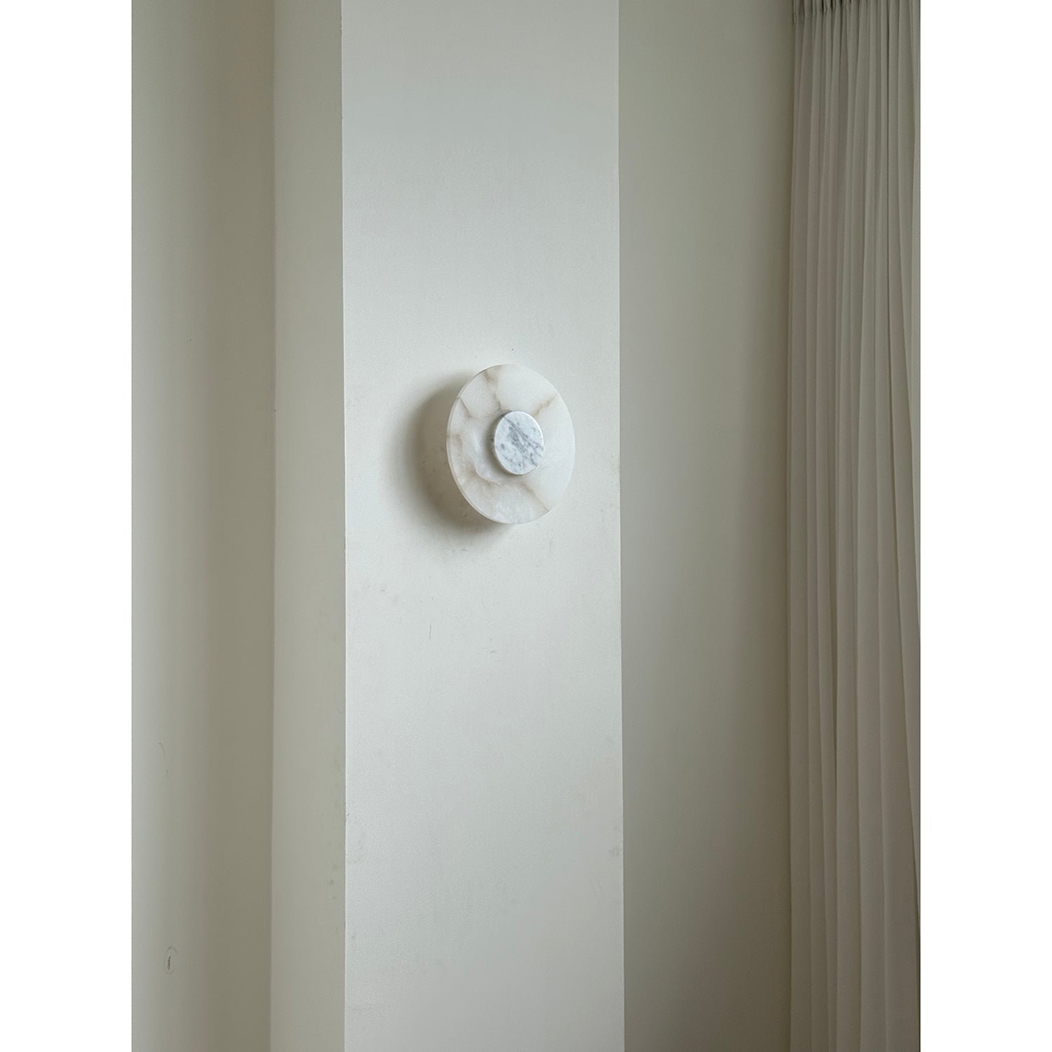 Clérachic rauduvyi wall lamp switched off on a pale wall pier next to a pleated floor-length curtain