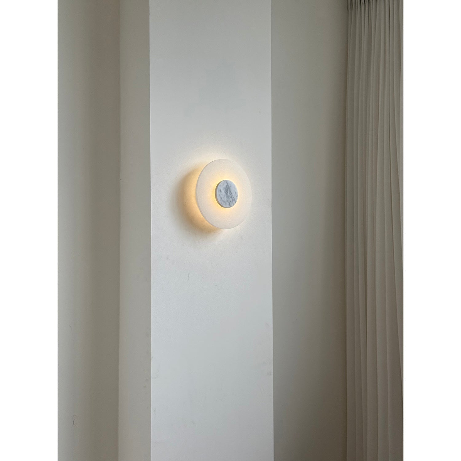 Clérachic rauduvyi wall lamp glowing on a plain interior wall, seen from across the room at eye level