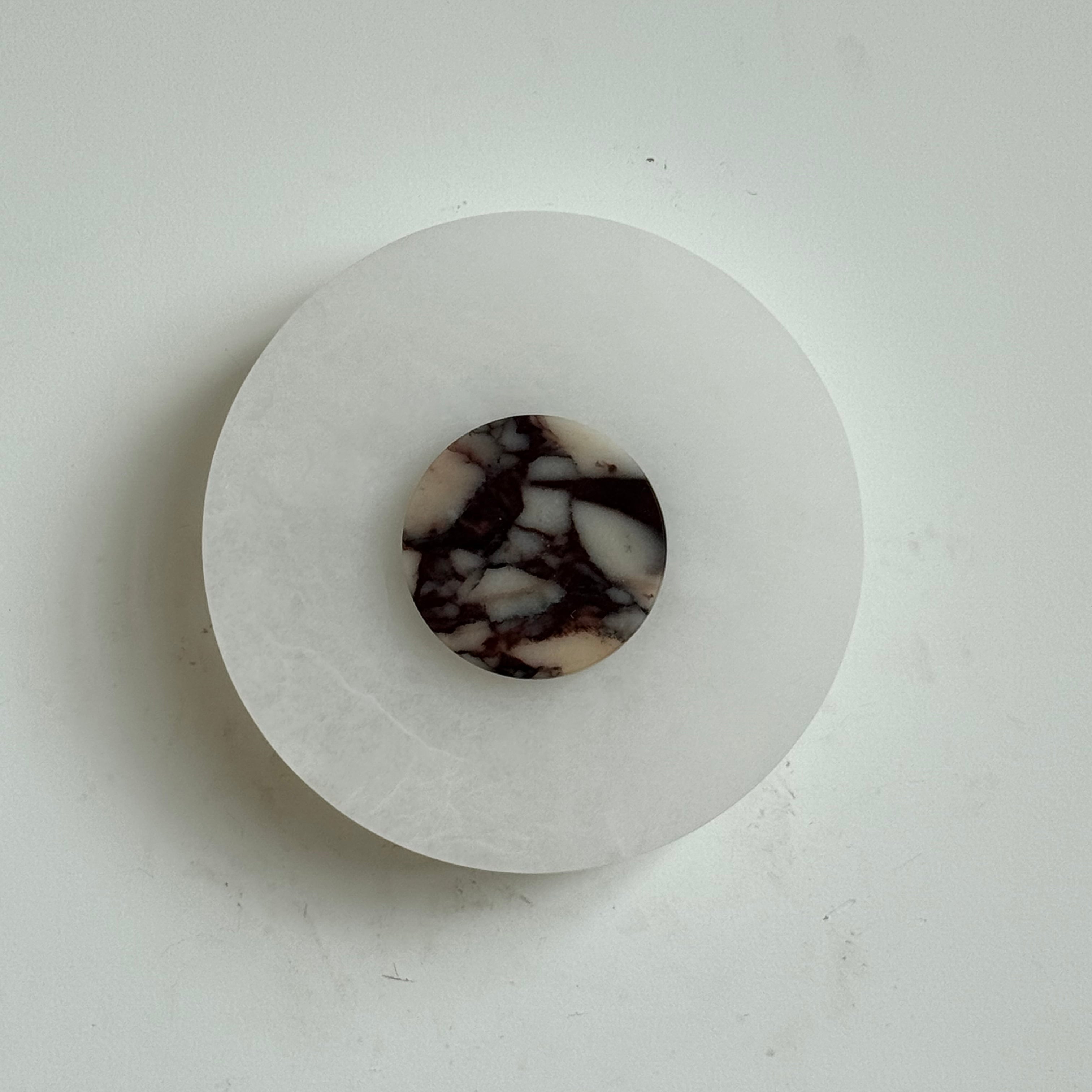 The Clérachic Rauduvyi wall lamp unlit, its violet-veined marble disc contrasting with the milky alabaster plate