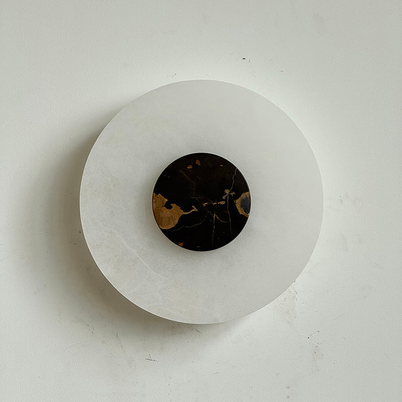 Clérachic wall-mounted Rauduvyi lamp shown off, the black and gold marble disc set against smooth alabaster