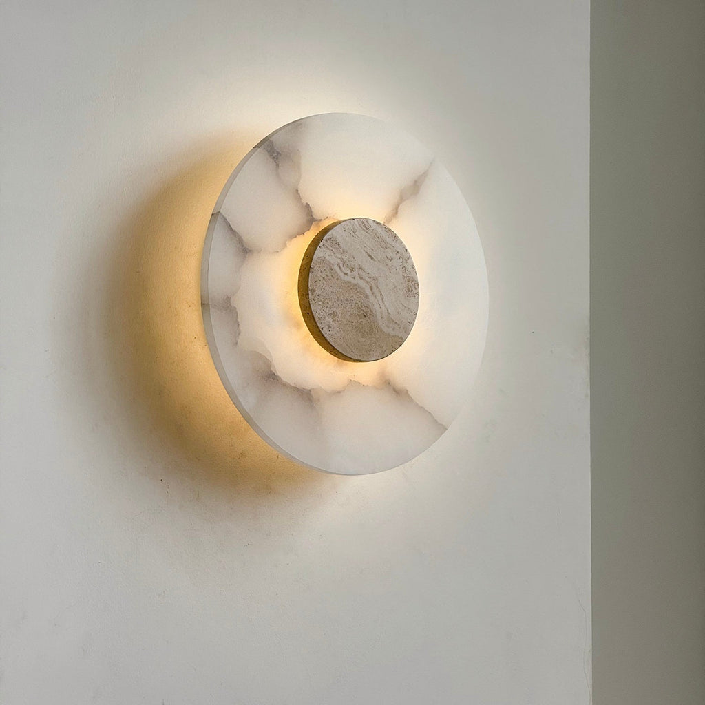 Clérachic rauduvyi wall lamp lit at an angle, the beige travertine disc framed by a halo of warm light
