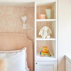 White plaster Kristy sconce above an upholstered headboard on blush blossom wallpaper in a child's room.
