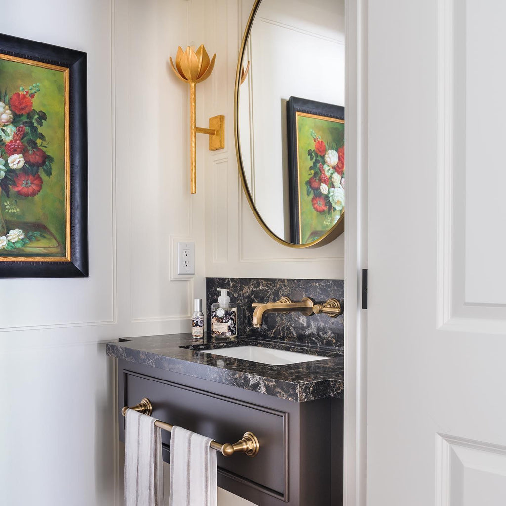 Gold-leaf Kristy sconce beside a round brass mirror in a panelled powder room with a marble vanity.