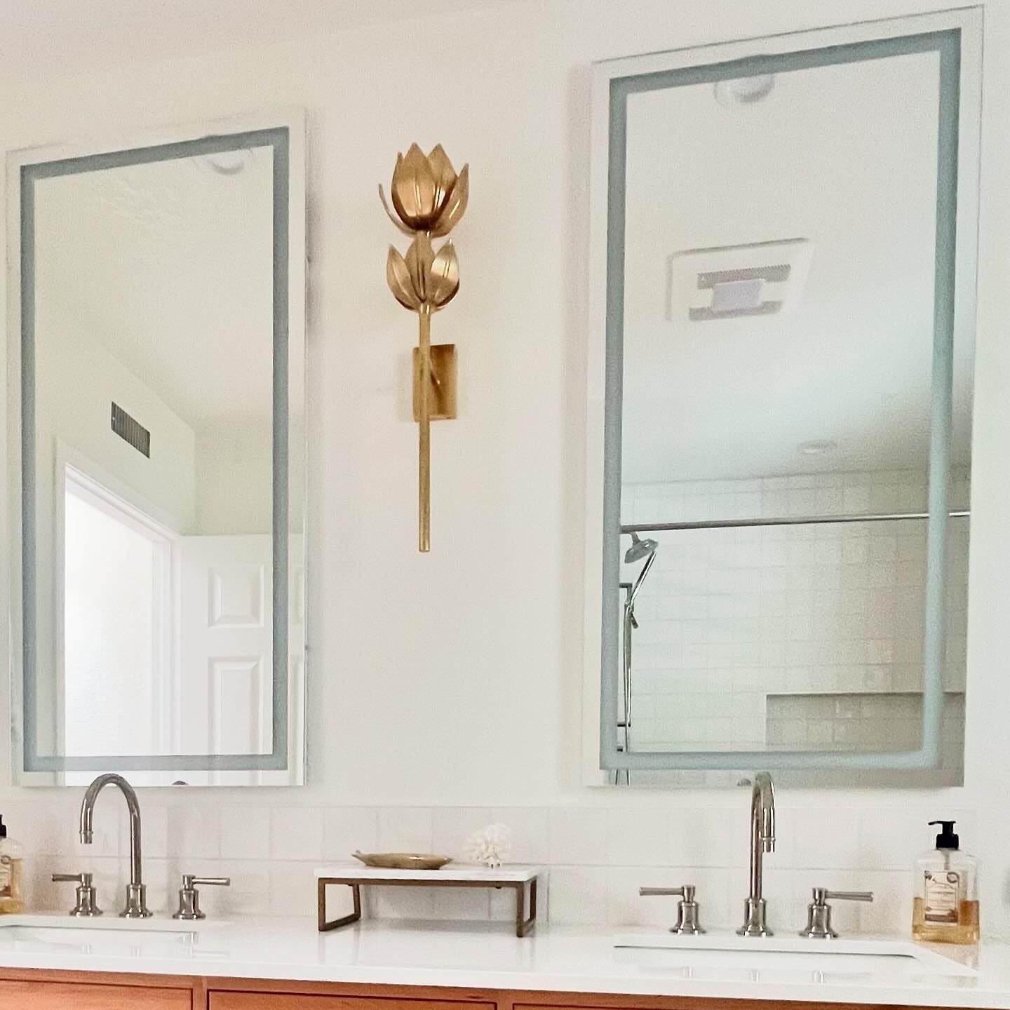Large gold Kristy sconce with two blooms mounted between twin mirrors over a double bathroom vanity.