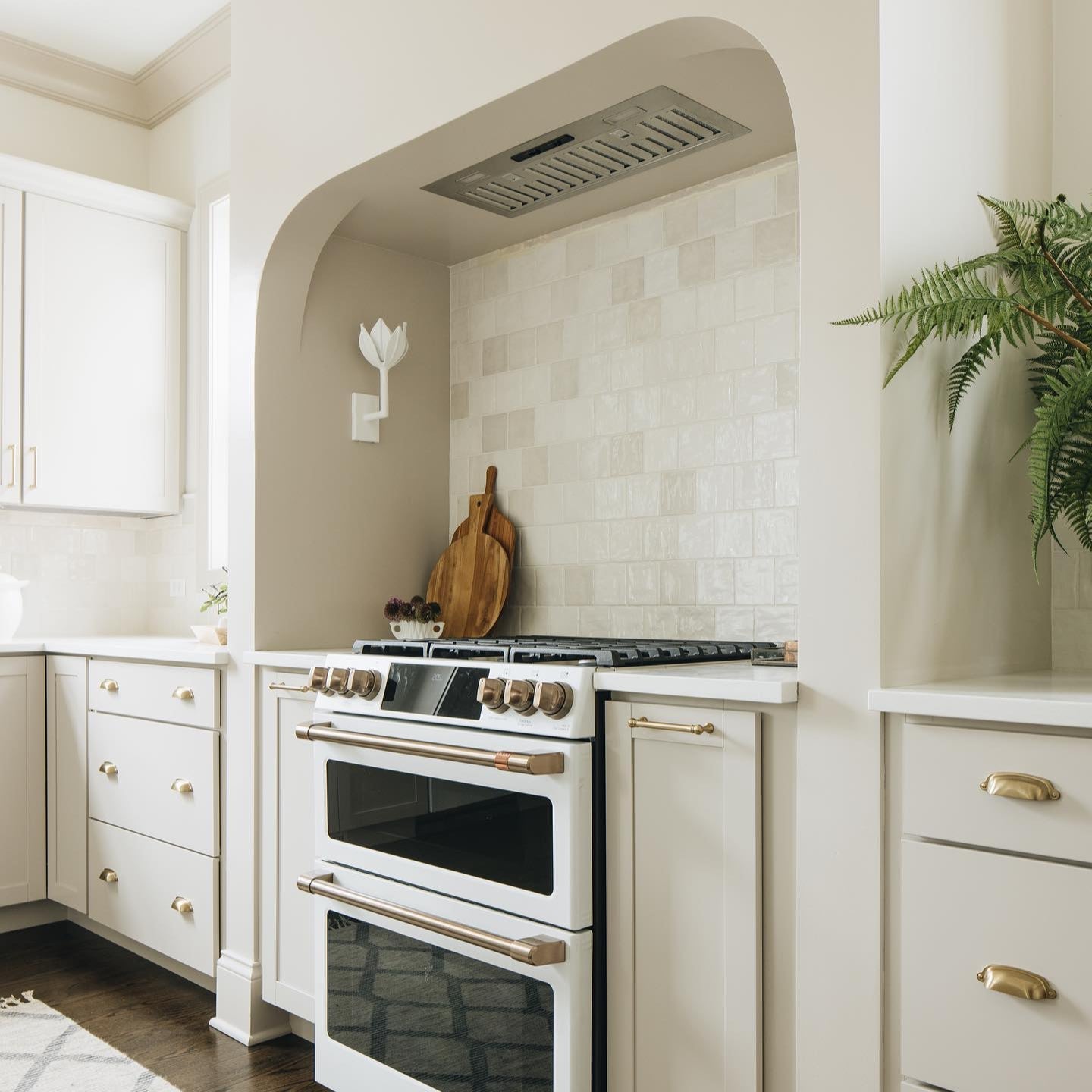 White Kristy sconce on the greige wall of an arched kitchen alcove above a cream range.